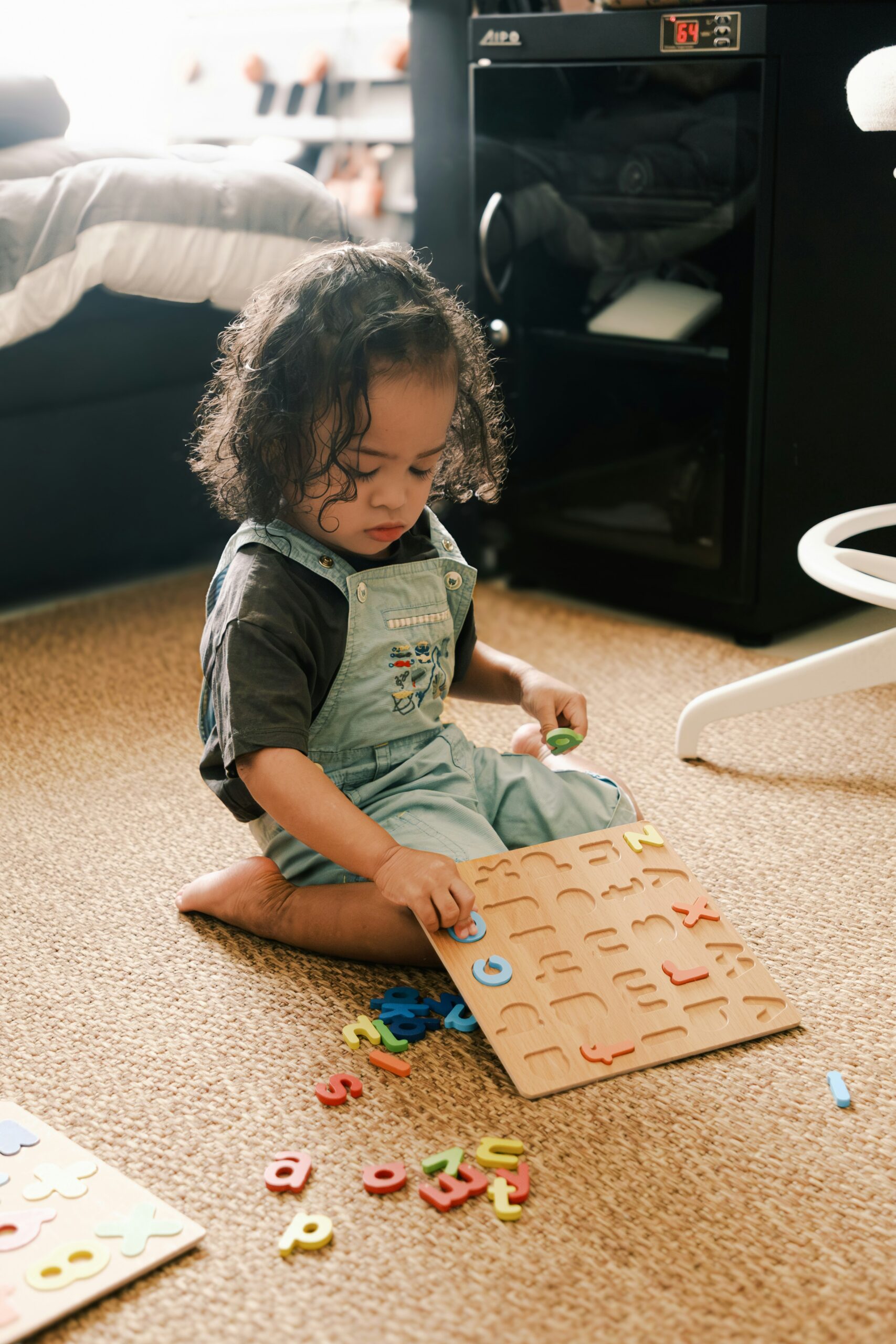 A young child plays with an alphabet puzzle on the floor